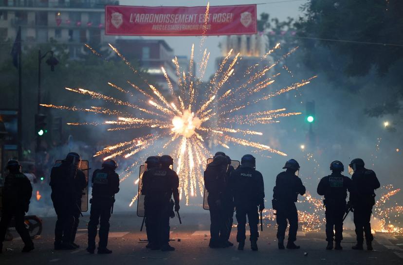 Fireworks light up the sky as police forces maintain order in Paris after PSG's Champions League victory.