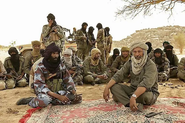 Des rebelles touaregs assis sur un tapis sous un arbre, entourés de combattants.